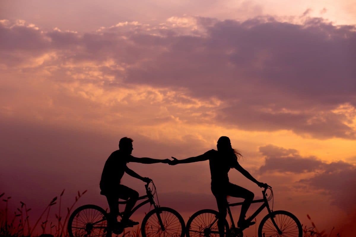 Couple reaching for each other while cycling at sunset